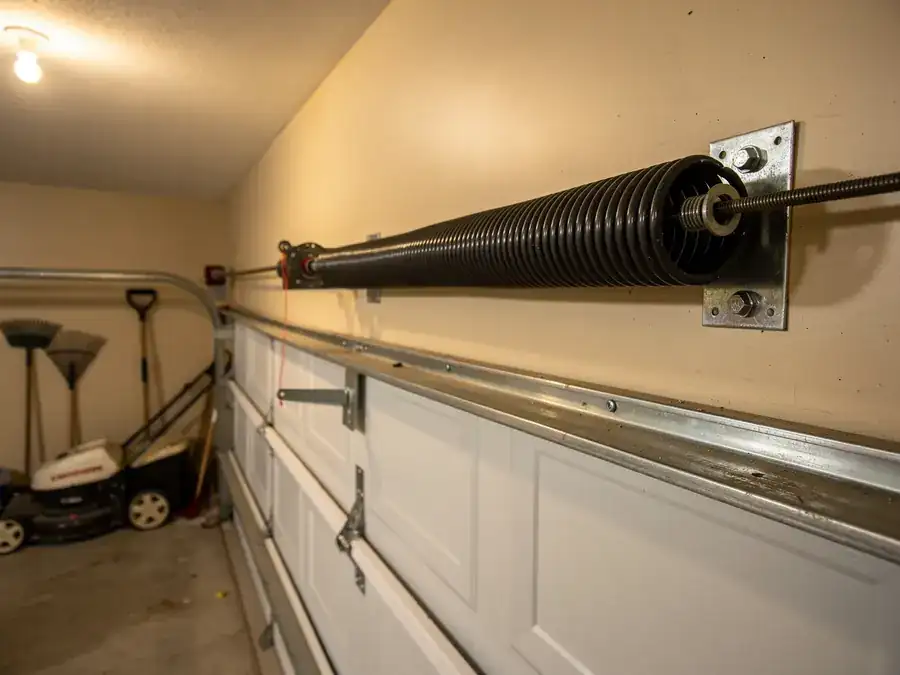 A torsion spring is mounted above a white garage door.