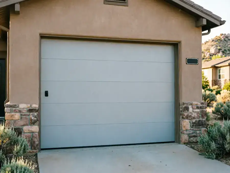 A light gray garage door with a black handle on a tan house.